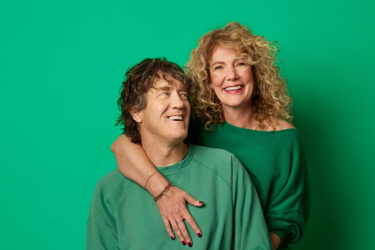 Man en vrouw in groene kleding lachen en omhelzen elkaar, symbool voor warme en speelse verbondenheid in een relatie